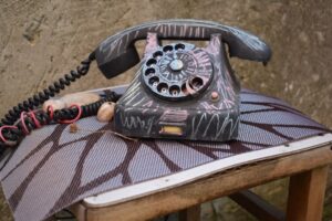 An old rotary dial telephone sits on a patterned cushion.