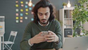 Man with long hair using a smartphone at desk.