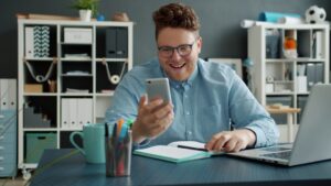 Man smiling while looking at his phone at desk